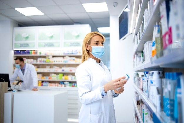 Farmacéutica con mascarilla y bata blanca con medicina en la farmacia durante la pandemia del virus corona.