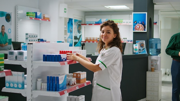 Farmacêutica sorridente examinando pacotes de pílulas para ajudar clientes com doenças e medicamentos prescritos. Empregado trabalhando na farmácia e olhando para medicamentos ou produtos farmacêuticos.