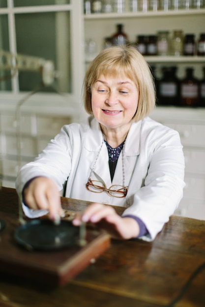 Farmacêutico de meia-idade loira sorridente, trabalhando com escalas vintage na farmácia