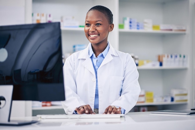 Farmacêutico digitando e mulher negra feliz no computador em farmácia farmácia ou loja Sorrir profissional médico e médico africano na internet para telessaúde e pesquisa para medicina