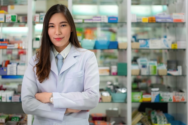 Farmacêutico fêmea novo asiático seguro com um sorriso amigável encantador que está com os braços cruzados na farmácia da farmácia. Medicina, farmácia, cuidados de saúde e conceito de pessoas.
