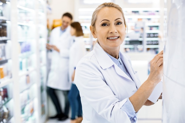 Farmacéutico femenino inspirado posando sobre fondo borroso y mirando a cámara