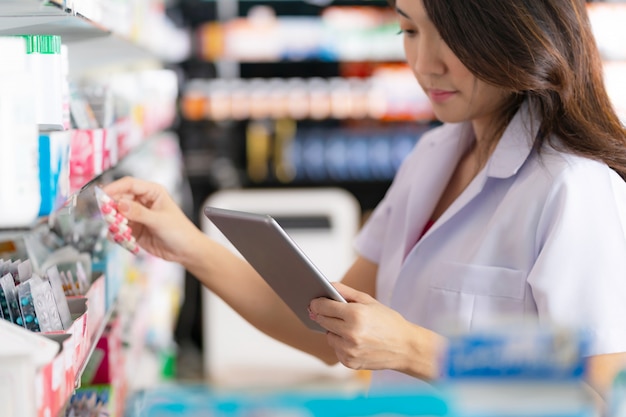 Foto farmacêutico feminino tomando um remédio da prateleira e usa tablet digital na farmácia