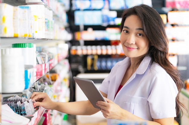 Farmacêutico feminino tomando um remédio da prateleira e usa tablet digital na farmácia