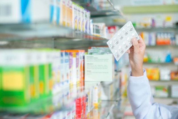 Farmacêutico feminino vestindo jaleco em uma farmácia moderna selecionando um medicamento