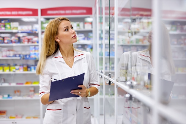 Farmacéutico joven buscando medicamentos en los estantes de las farmacias