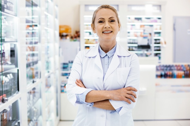 Farmacéutico mujer alegre cruzando las manos y posando sobre fondo borroso