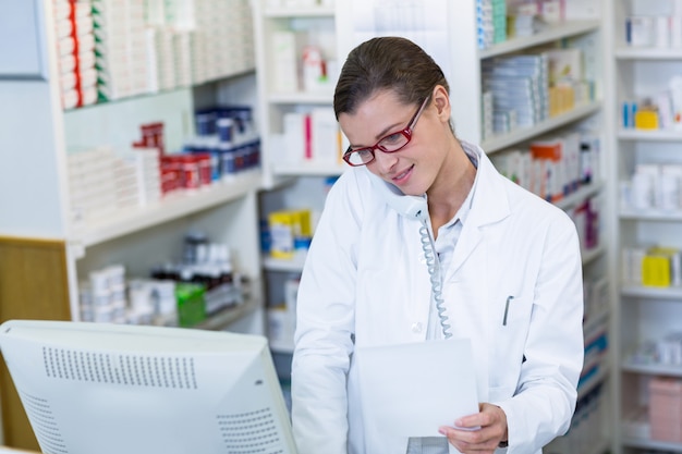 Farmacéutico con papel de receta mientras habla por teléfono