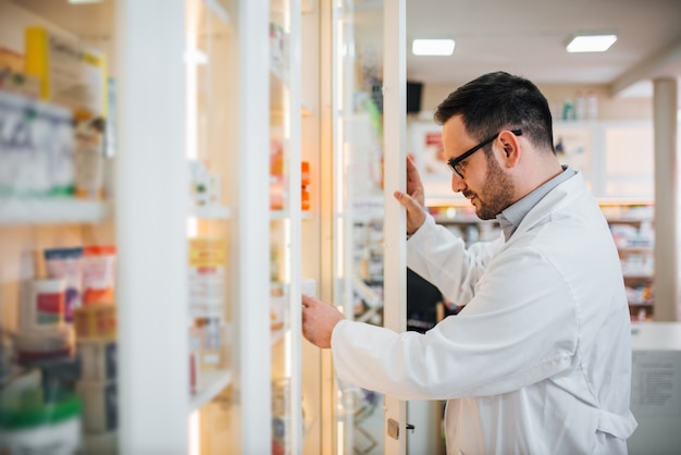 Farmacéutico que comprueba para saber si hay medicina en estante en la farmacia.