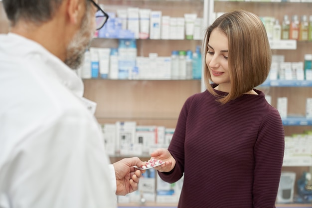 Farmacéutico que ofrece un blister de píldoras al cliente.