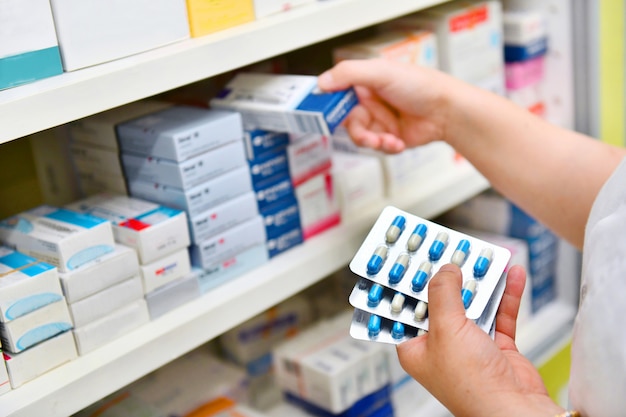 Foto farmacéutico que sostiene la caja de la medicina y el paquete de la cápsula en farmacia farmacia.