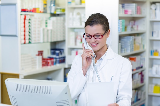 Farmacêutico segurando papel de prescrição enquanto fala no telefone