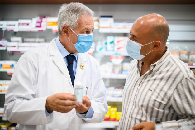 Farmacêutico sênior lidando com um cliente, ambos usando máscaras devido ao coronavírus