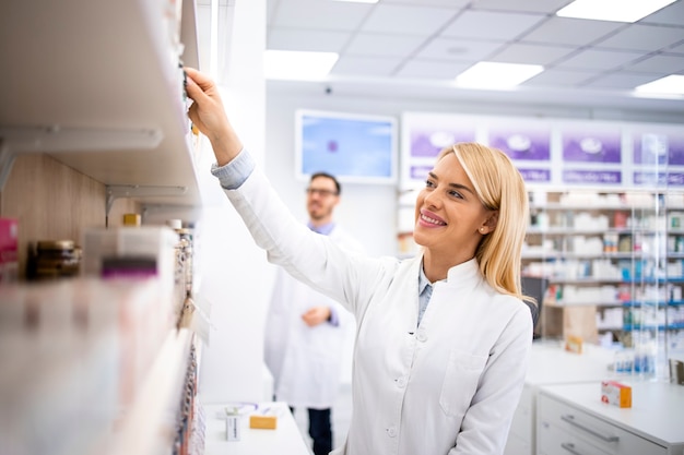 Farmacéutico de sexo femenino que trabaja en la tienda de la farmacia que toma la medicina del estante.