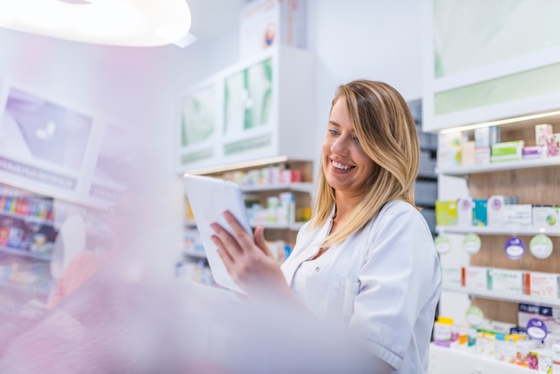 Farmacêutico trabalhando com um tablet na farmácia segurando-o na mão enquanto lê informações