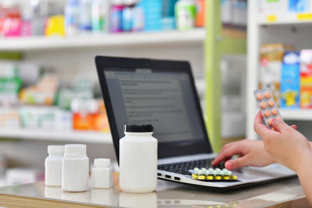 Farmacêutico usando o laptop do computador na farmácia ou farmácia. mão segurando o pacote de remédios e chave a ordem de prescrição.