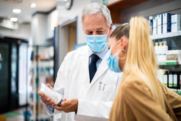 Farmacista sénior tratando con un cliente ambos con máscaras debido al coronavirus