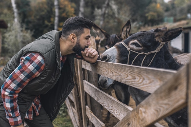 Foto farmaer de pelo oscuro de pie cerca del puesto con burros