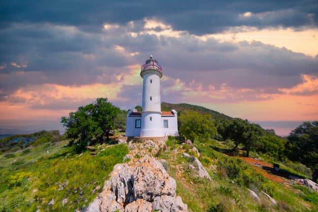 Foto un faro blanco está en una colina con árboles y una colina en el fondo