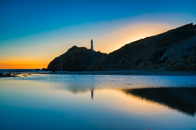 El faro de CastlePoint y los primeros signos de la luz solar reflejados en las tranquilas aguas de la laguna cuando sale el sol al amanecer