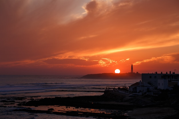 Faro con colorido atardecer con sol en el horizonte