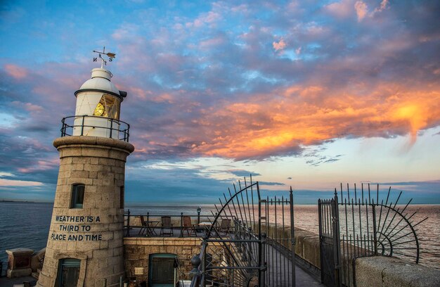 Faro por el mar contra el cielo durante la puesta de sol