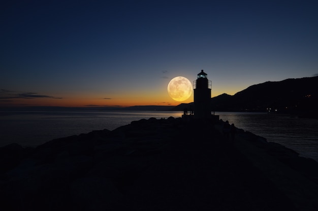 faro en la noche con increíble luna llena sobre el mar