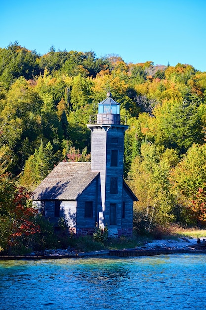 Faro en la orilla del lago Superior con ventanas tapiadas y bosque verde más allá