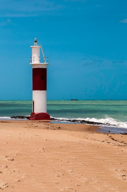 Faro en la playa por el mar contra el cielo