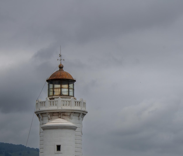 FARO DEL PUERTO PESQUERO BLANCO Y AMARILLO CON VENTANAS EN UN DÍA NUBLADO DE VERANO