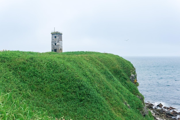 Farol abandonado em um promontório gramado alto acima de um mar nevoento