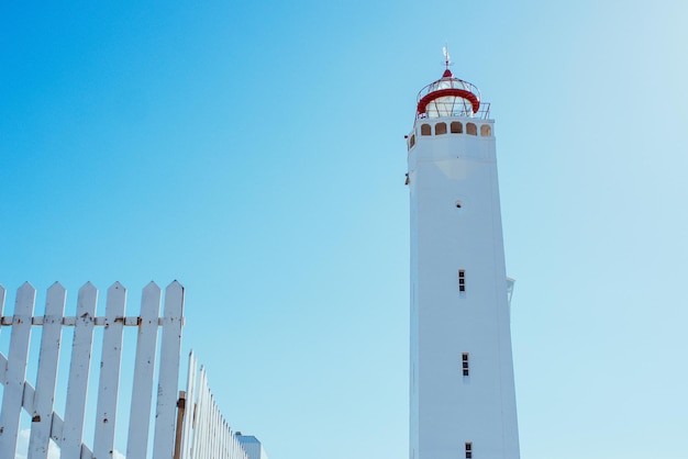 farol branco com cerca branca no fundo do céu azul perto do mar