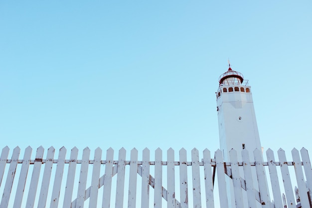 farol branco com cerca branca no fundo do céu azul perto do mar