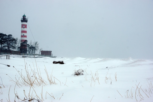 Farol na baía com listras vermelhas, visibilidade ruim devido à queda de neve