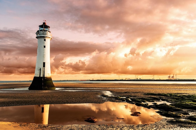 Farol na praia contra o céu nublado durante o pôr-do-sol