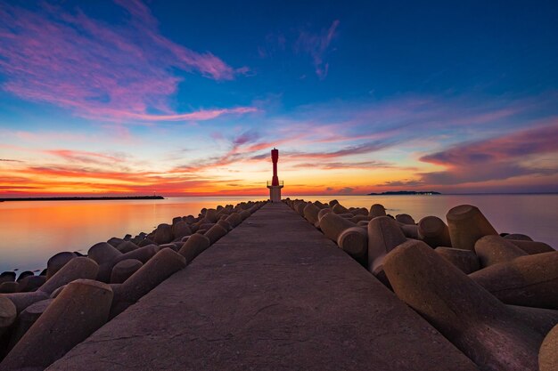 Foto farol no cais no mar contra o céu durante o pôr do sol