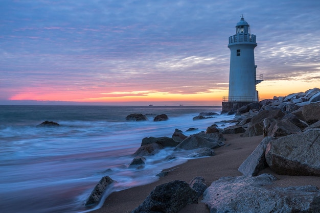 Farol pelo mar contra o céu durante o pôr-do-sol