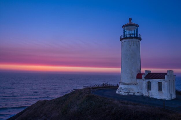 Farol pelo mar contra o céu durante o pôr-do-sol