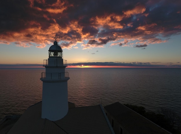 Farol pelo mar contra o céu durante o pôr-do-sol