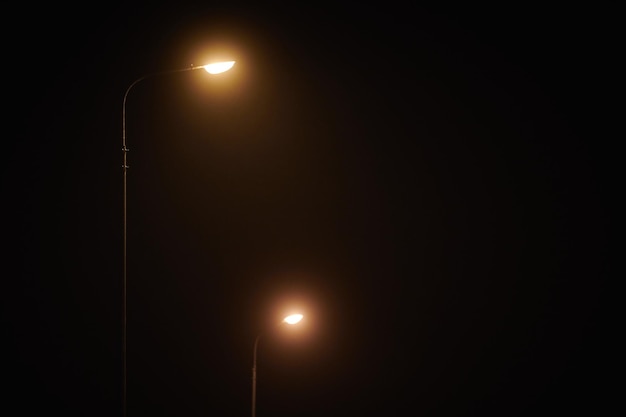 La farola de dos noches brilla con una tenue y misteriosa luz amarilla a través de la niebla nocturna en una noche tranquila