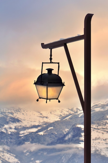 Farola frente a una hermosa puesta de sol en la montaña nevada