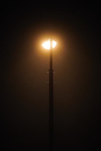 Una farola nocturna brilla con una tenue y misteriosa luz amarilla a través de la niebla nocturna