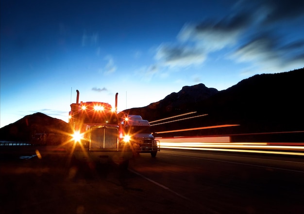 Faros iluminados de un semirremolque contra el cielo al anochecer