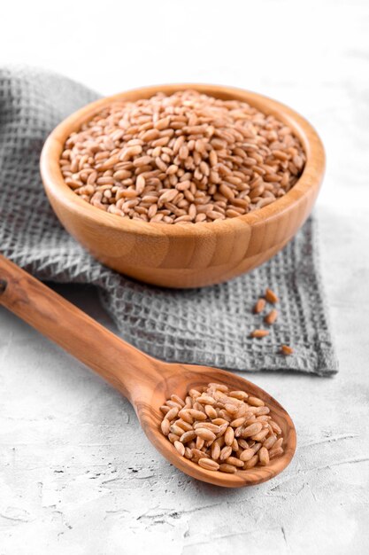 Foto farro de espelta crudo de grano entero en un cuenco de madera sobre una mesa de piedra gris