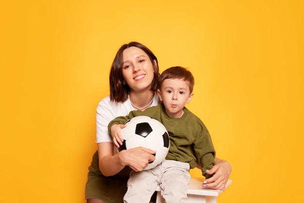 Fãs de futebol feliz jovem mãe com seu filho fofo posando isolado em amarelo brilhante