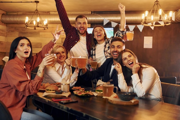 Fãs de futebol Grupo de jovens amigos sentados juntos no bar com cerveja