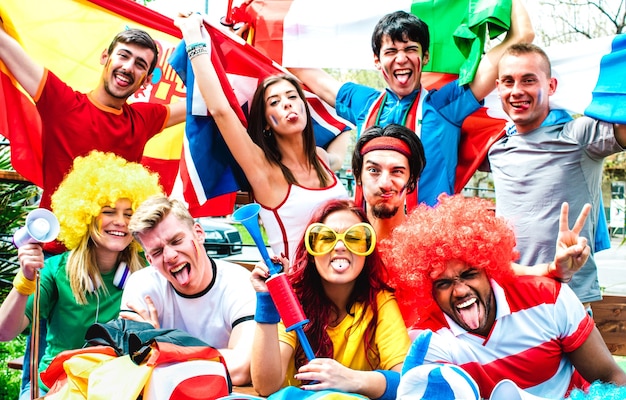 Fãs de jovens torcedores de futebol torcendo com bandeiras internacionais em uma partida de futebol - Pessoas felizes com camisetas multicoloridas se divertindo ao ar livre - Conceito de campeonato de esporte em filtro vívido quente