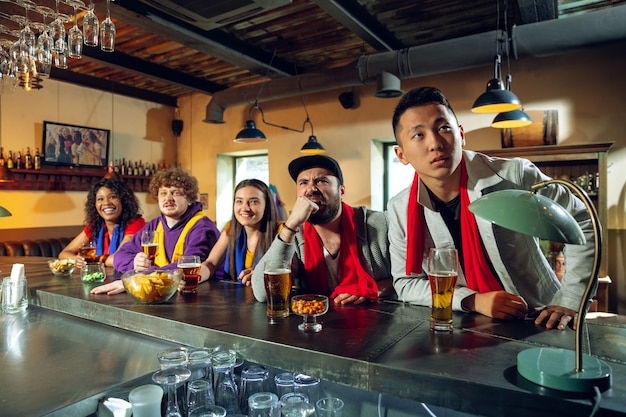 Fãs do esporte torcendo em bar, pub e bebendo cerveja enquanto o campeonato, a competição está acontecendo. grupo multiétnico de amigos animado assistindo a tradução. emoções humanas, expressão, conceito de apoio.