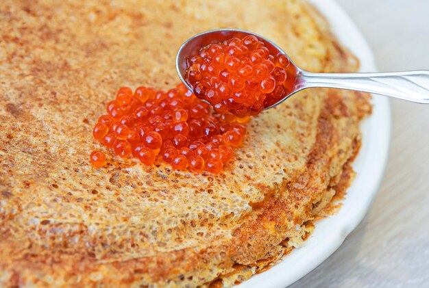 Faschingskonzept. Stapel Crêpes oder Pfannkuchen mit rotem Lachskaviar im Löffel an der Spitze.