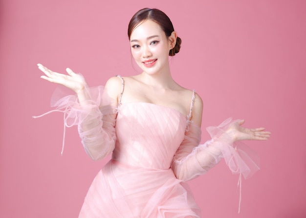 Fascinante divertido alegre jovem mulher da Ásia usa doce vestido de flor rosa pose estendendo as mãos isoladas em fundo rosa claro pastel retrato de linda senhora no estúdio